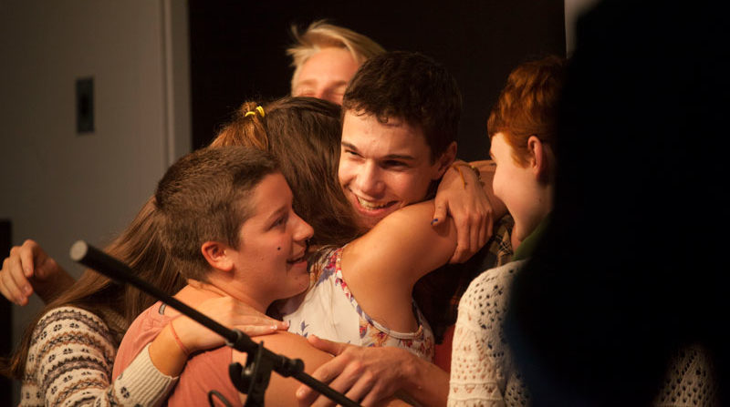 High school students hugging in a group in front of a microphone