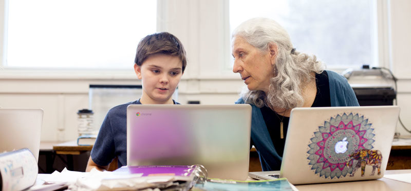 A teacher assisting a student while they work on their laptops